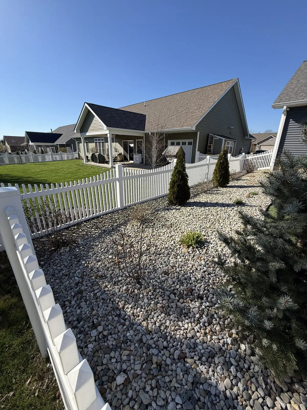 White vinyl picket fence with river rock front yard landscaping in Bloomington, IN