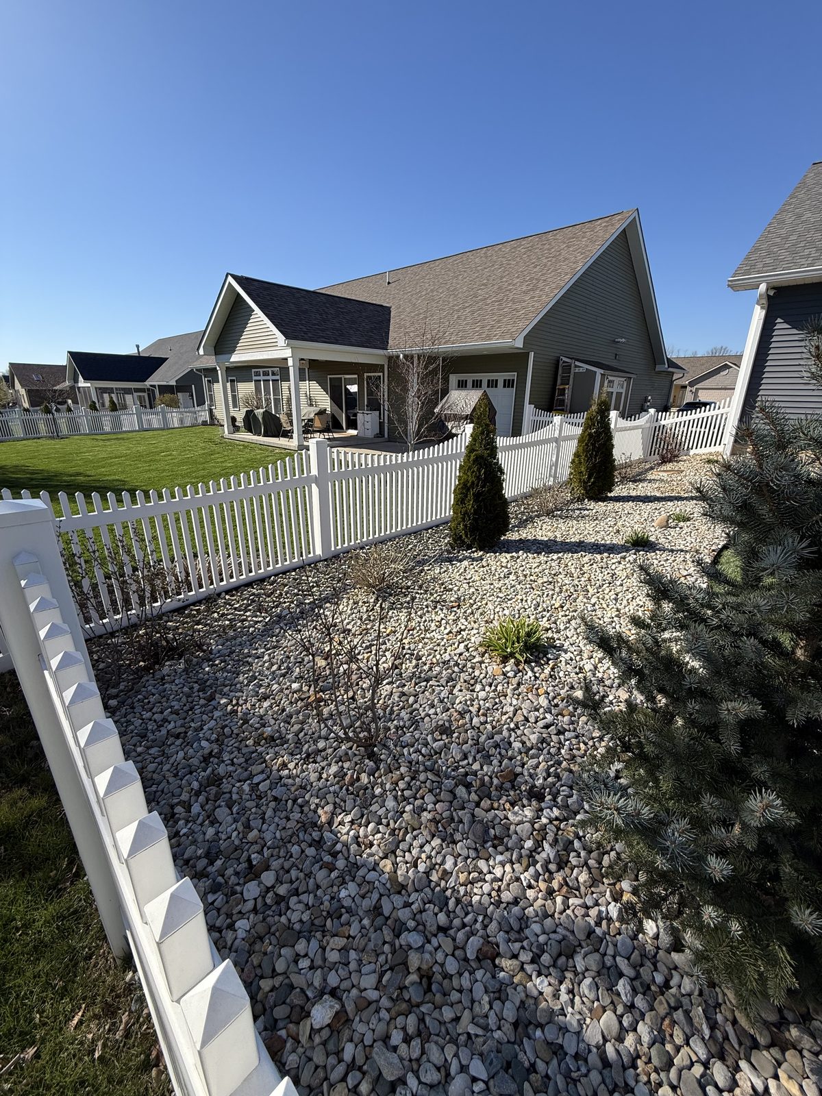 White vinyl picket fence with river rock front yard landscaping in Bloomington, IN